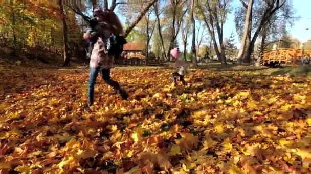 Aktives Familienspiel zwischen Herbstblättern im Park. Mutter mit kleinen Kindern — Stockvideo