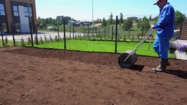 Ev bahçesinde çim silindirini toprağın içinden iten adam. Gimbal hareket çekimi