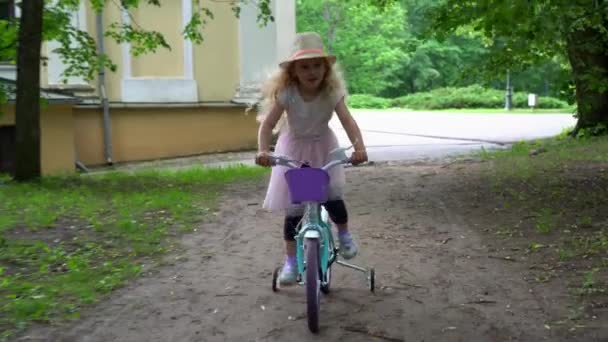 Söt liten kvinnlig modell i rosa klänning rida cykel på fyra hjul. Gimbal shot — Stockvideo