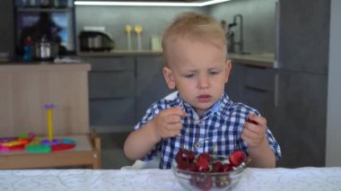 Mutfakta oturan kiraz yiyen erkek bebek. Masada tabakta kiraz. Gimbal