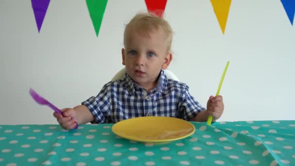 포크와 칼을 손에 들고 테이블을 치는 어린 소년. 짐벌 샷. — 비디오