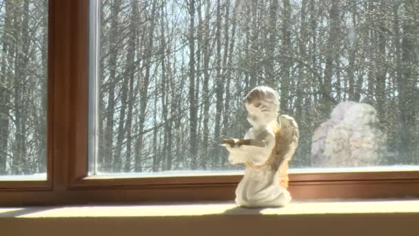 Estatua de ángel pequeño rezar con libro en el alféizar de la ventana iluminado con sol — Vídeos de Stock
