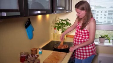 hamile kadın pişirme tavada yemek karıştırma ve kameraya bakarak gülümseme