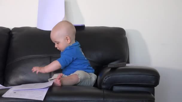 Aranyos baba fiú játszik a dokumentumokkal papírok a kanapén — Stock videók
