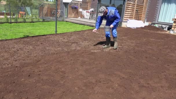 Κηπουρού άνθρωπος εξάπλωση χόρτο σπόρος με το χέρι για τέλειο γκαζόν. Στατικός πυροβολισμός. — Αρχείο Βίντεο