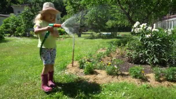 Gardener garoto loiro com chapéu segurando pulverizador de água e flores de pulverização. Gimbal. — Vídeo de Stock