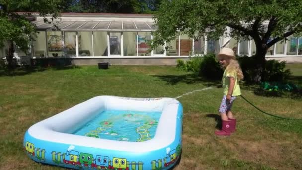 Chica rubia llenar piscina inflable con manguera de agua en casa de campo. Movimiento del cardán — Vídeo de stock