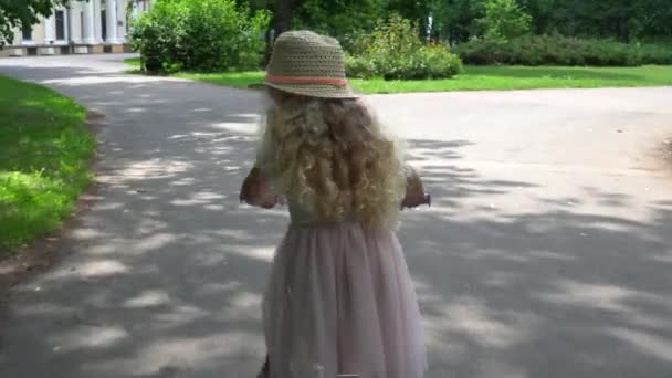 Elegancka dziewczyna dziecko z kapeluszem i różową sukienkę jazda na rowerze w plenerze — Wideo stockowe