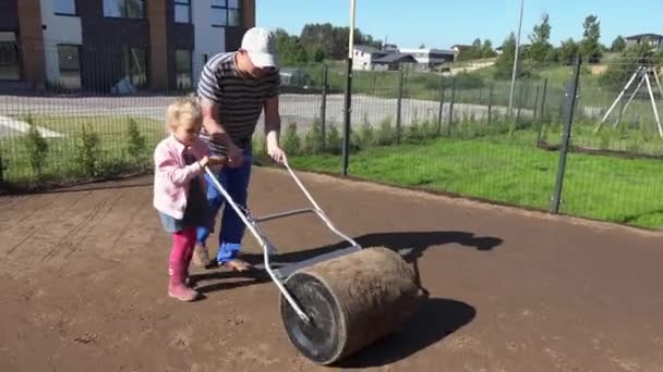 Vater und Helfermädchen ebenerdig mit Rollator im Stadthallenhof. Rasensaat. — Stockvideo