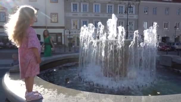 Entzückendes blondes Mädchen, das vor dem Brunnen steht. Handschuss — Stockvideo