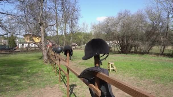 馬のライダーの保護ヘルメットは、安定したパドックフェンスにハングアップします。ジンバルムーブメント — ストック動画