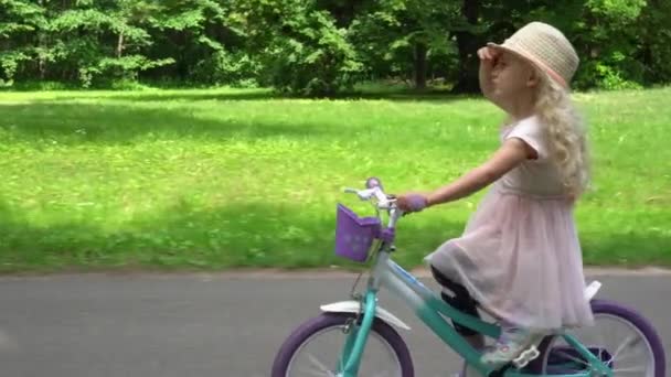 Entzückendes kaukasisches Mädchen mit Hut fährt Fahrrad im Stadtpark. Gimbale Bewegung — Stockvideo