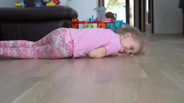 Petite fille mignonne avec des cheveux blonds rouler sur le sol vers la caméra. Gimbal motion shot — Video