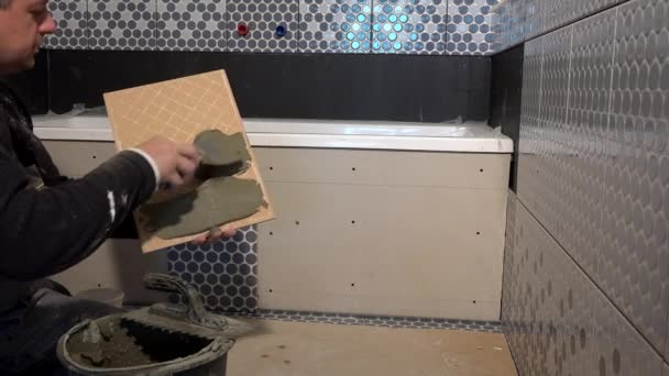 Arbetare man med murslev applicera lim på baksidan av kakel — Stockvideo