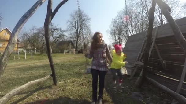 Mother with girl child swinging on retro wooden swing in early spring — Stock Video