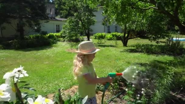 Söt liten flicka vatten blommor säng med slang sprinkler spruta. Gimbal rörelse — Stockvideo