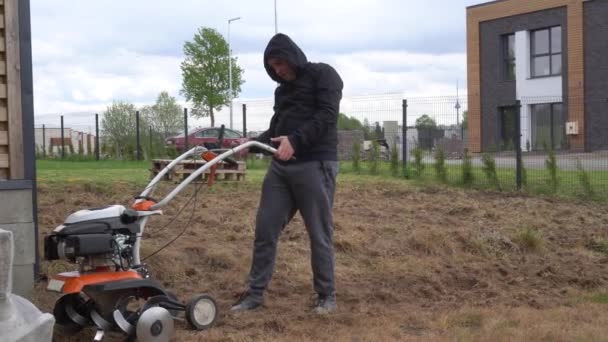 Schwacher Mann startet Motor eines Kultivators und arbeitet kaum im Stadthallenhof — Stockvideo