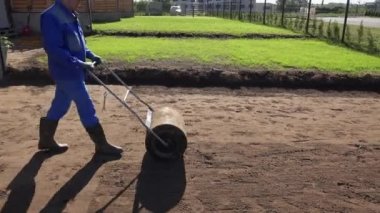 Peyzajcı adam çim tohumlama sonra toprak toprak sertleştirmek için rulo kullanıyor. El