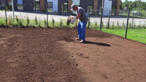 Trabalhador com balde cheio de terra fértil enriquecer o solo para a semeadura do gramado no quintal — Vídeo de Stock
