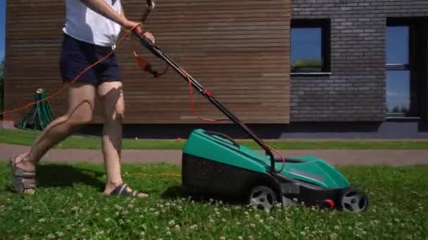 民間の家の庭で芝刈り機草を刈る女性。ジンバル側フォロー — ストック動画
