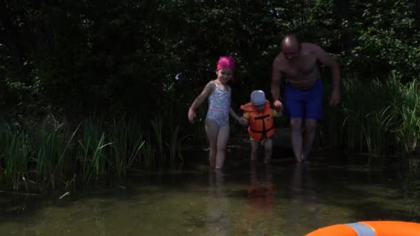 Батько і дочка ведуть маленького сина, що блукає у воді. хлопчик з рятувальною жилетною курткою — стокове відео