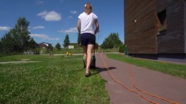 Evinin arka bahçesinde çim biçen bir kadın. Gimbal hareketi geri izleyin