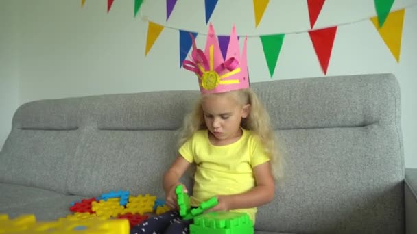 Pequeña princesa con corona construir algo de piezas de colores en el sofá — Vídeos de Stock