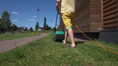çim biçme makinesi ile bahçıvan adam ev bahçesinde kaldırım yakınında yeşil çim kesiyor