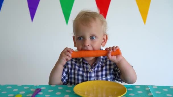 Lindo niño sosteniendo zanahoria con ambas manos y morderla. Movimiento de cardán — Vídeos de Stock