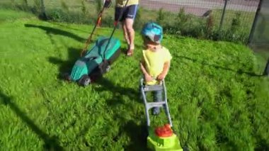 Babasının önünde oyuncak çim biçme makinesi ile Mutlu aktif yürümeye başlayan çocuk. Gimbal hareketi
