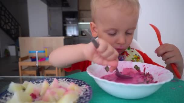 Lindo bebé comiendo sopa de remolacha y papas con dos cucharas — Vídeo de stock