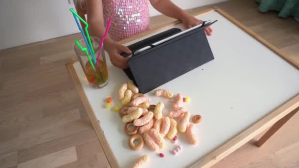 Menina irreconhecível criança brincando com computador tablet perto da mesa cheia de doces — Vídeo de Stock