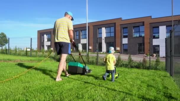 Grappig jongens vader en zoon snijden gras in prive-appartement werf. Gimbal Motion — Stockvideo