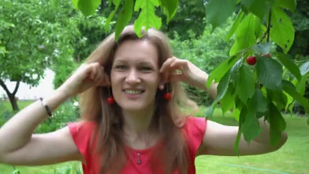 Mujer juguetona posan con aretes de cereza natural en el jardín. Movimiento del cardán — Vídeo de stock