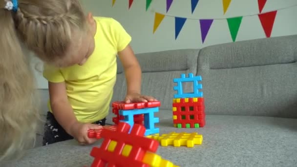 Θηλυκό παιδί που συνδέει πολύχρωμα εξαρτήματα κατασκευής στον καναπέ. Κίνηση αναρτίδα — Αρχείο Βίντεο