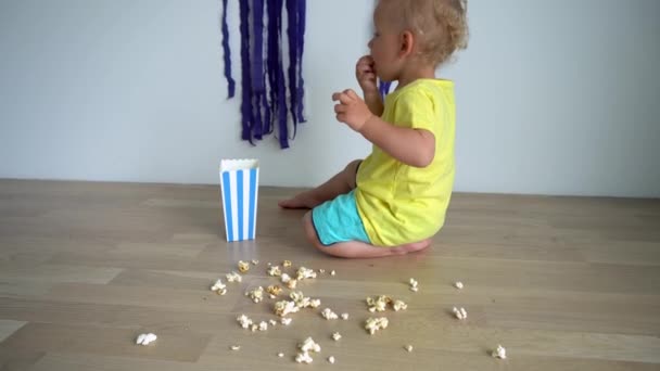 Kisfiú étkezési popcorns és ezzel rendetlenség a padlón otthon. Gimbal mozgás — Stock videók