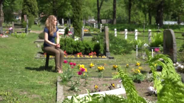 A rapariga da mágoa encolhe perto do túmulo do pai marido no cemitério. 4K — Vídeo de Stock