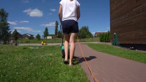 Jardinero chica con cortacésped está cortando hierba verde en casa patio trasero — Vídeo de stock