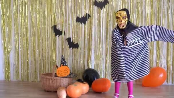 Ребенок в страшной маске на Хэллоуин и костюме заключенного пугает от камеры. 4K — стоковое видео