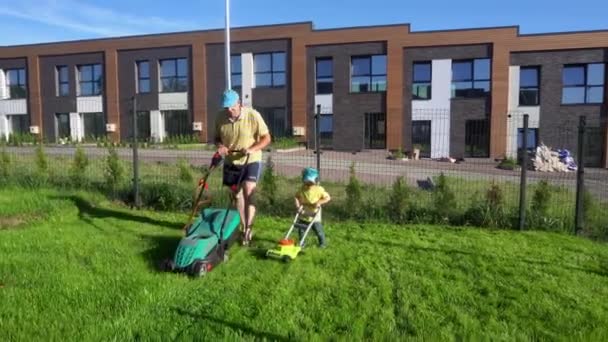 Kärleksfull far arbetar med liten son pojke på gården med gräsklippare. Gimbal följer — Stockvideo