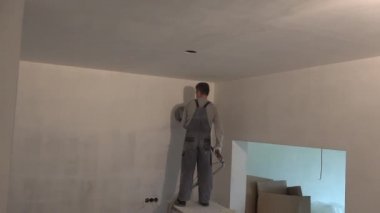 Yeni apartman dairesinde öğütücü makineli bir adam duvar boyuyor.