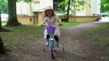 Pembe elbiseli dört tekerlekli bisiklet süren zarif bir bayan çocuk modeli. Gimbal atışı.