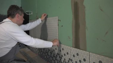 Orta yaşlı adam banyoda duvar döşeme ve seviyelendirme aracı ile seviye kontrol