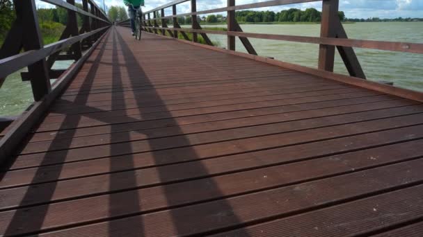 Hombre irreconocible en bicicleta cruzando el lago en un puente de madera. Transporte saludable — Vídeos de Stock