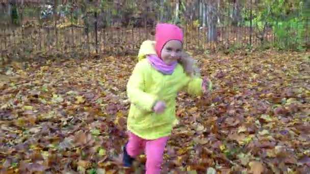 Активная девочка бежит после движения камеры на желтых осенних листьях в парке — стоковое видео