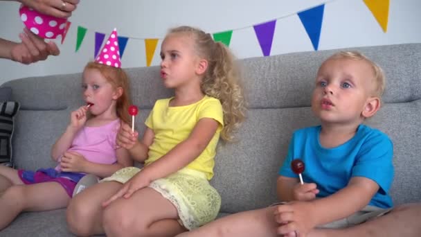 Moederhanden zetten feestmutsen op kinderhoofden. verjaardagsfeestje. camerabeweging — Stockvideo