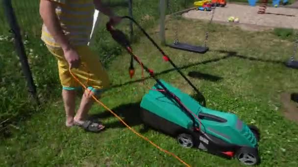 Hombre trabajador cortar hierba con cortacésped en casa patio cerca de swing en patio de recreo — Vídeo de stock