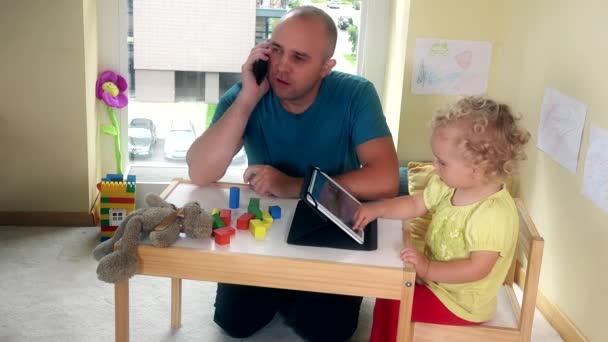 Padre hablar teléfono y bebé utilizar tableta de medios en la sala de estar. 4K — Vídeo de stock