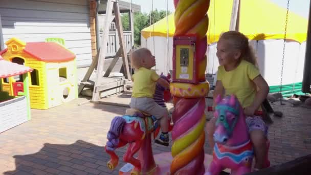 Joyeux enfants sur le manège à cheval dans l'aire de jeux. Mouvement du cardan — Video