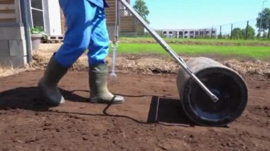 Toprak toprak silindiriyle çalışan çizmeli bir işçi. Gimbal paralel atış.